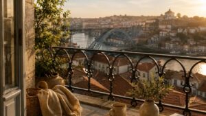 Terraço com manta, caneca, vaso e livro sobre uma mesa, com vista ampla sobre o rio, a ponte e a cidade ao pôr do sol, associado a CBD no Porto.
