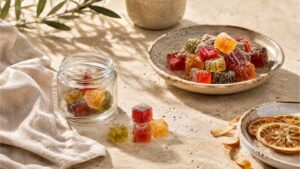 Frasco e prato com gummies coloridas, junto a elementos decorativos e fatias secas de citrinos, numa imagem sobre Gummies CBD Portugal.